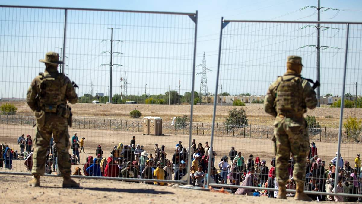 Migrantes esperan en una fila junto a una valla fronteriza mientras miembros de la Guardia Nacional de Texas los vigilan, en El Paso, el 10 de mayo de 2023