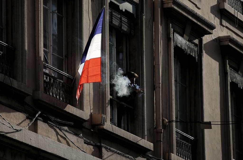 ARCHIVO - Un hombre fuma junto a una bandera francesa colgada de una ventana en Lyon, Francia, el viernes 27 de noviembre de 2015