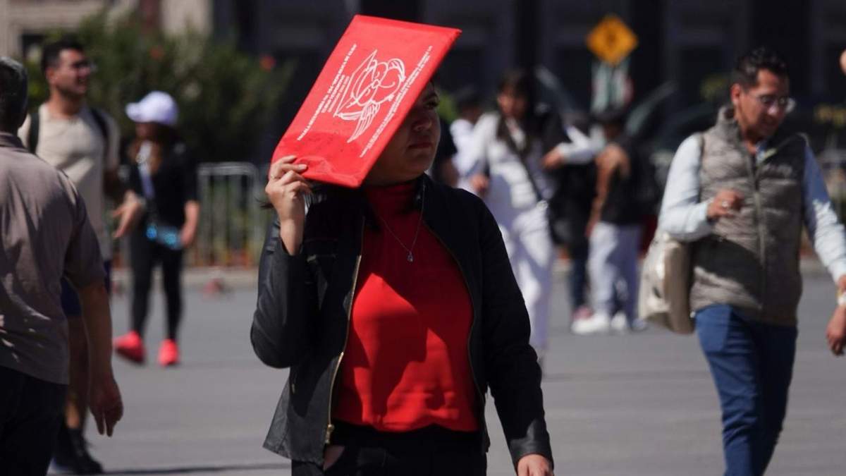 Una mujer se cubre de los rayos del sol con un folder en el Zócalo capitalino