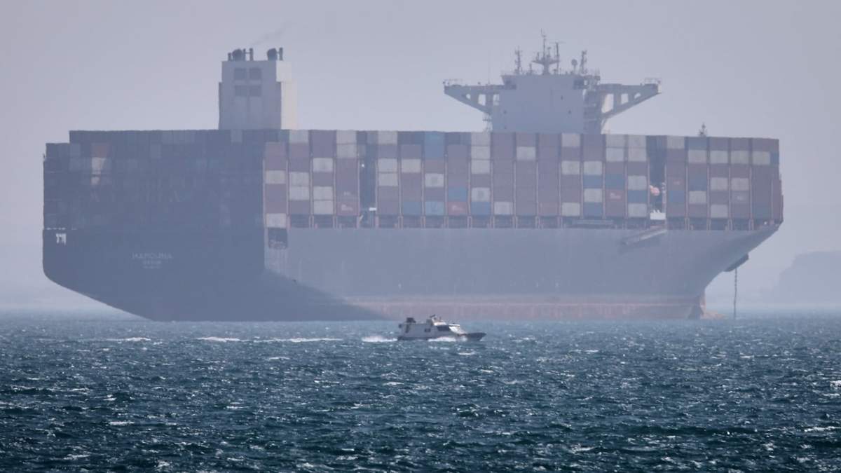 Un barco portacontenedores se ve fondeado mientras una lancha pasa por delante en el estrecho de Ormuz, cerca de Bandar Abbas, Irán, el sábado 2 de mayo de 2026