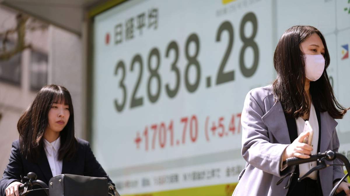 Mujeres en bicicleta pasan frente a pantallas que muestran el índice Nikkei 225 de Japón en Tokio, el martes 8 de abril