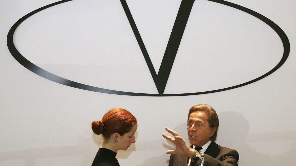 En esta imagen de archivo, el diseñador de moda italiano Valentino (derecha), bajo el logo de su marca, responde preguntas de un reportero antes de la presentación de su colección de Alta Costura Primavera-Verano 2008, el 23 de enero de 2008, en París