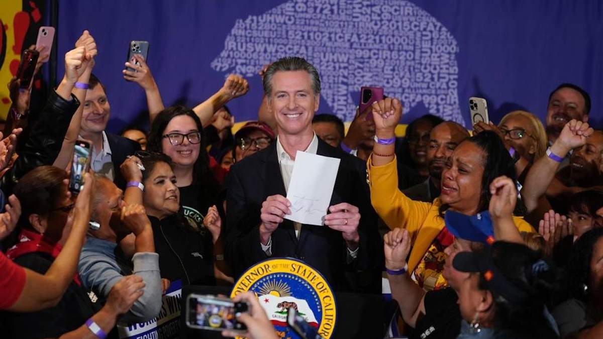 El gobernador de California, Gavin Newsom, muestra el proyecto de ley sobre comida rápida rodeado de trabajadores de ese sector