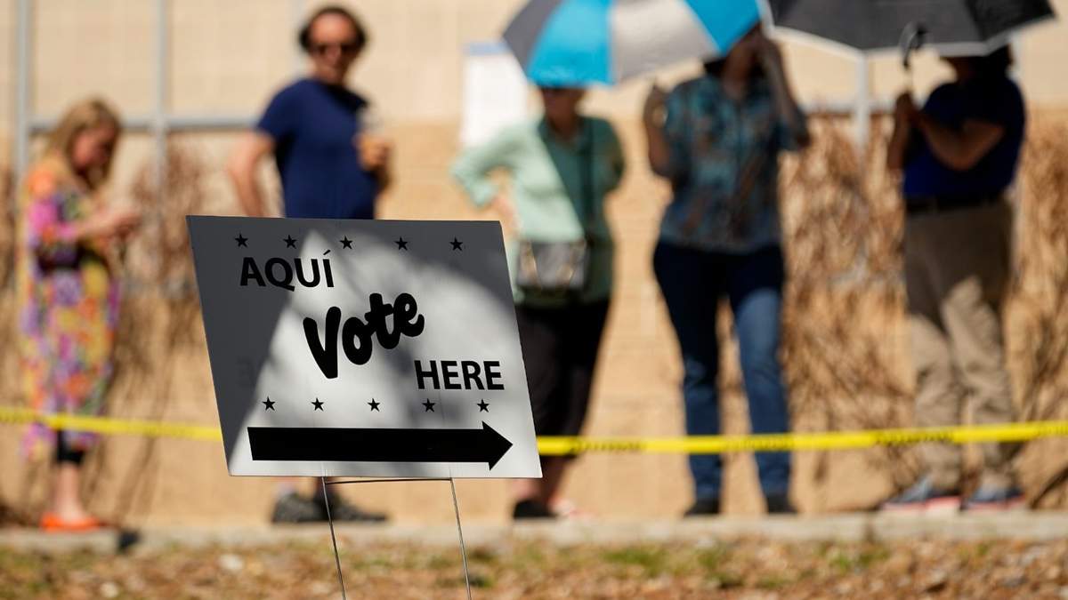 Ciudadanos usan sombrillas para cubrirse del sol mientras esperan formados en un centro de votación