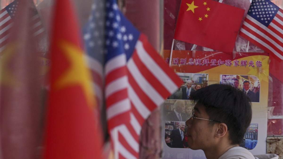 Un hombre entra en una tienda que exhibe banderas de China y Estados Unidos, en Pekín