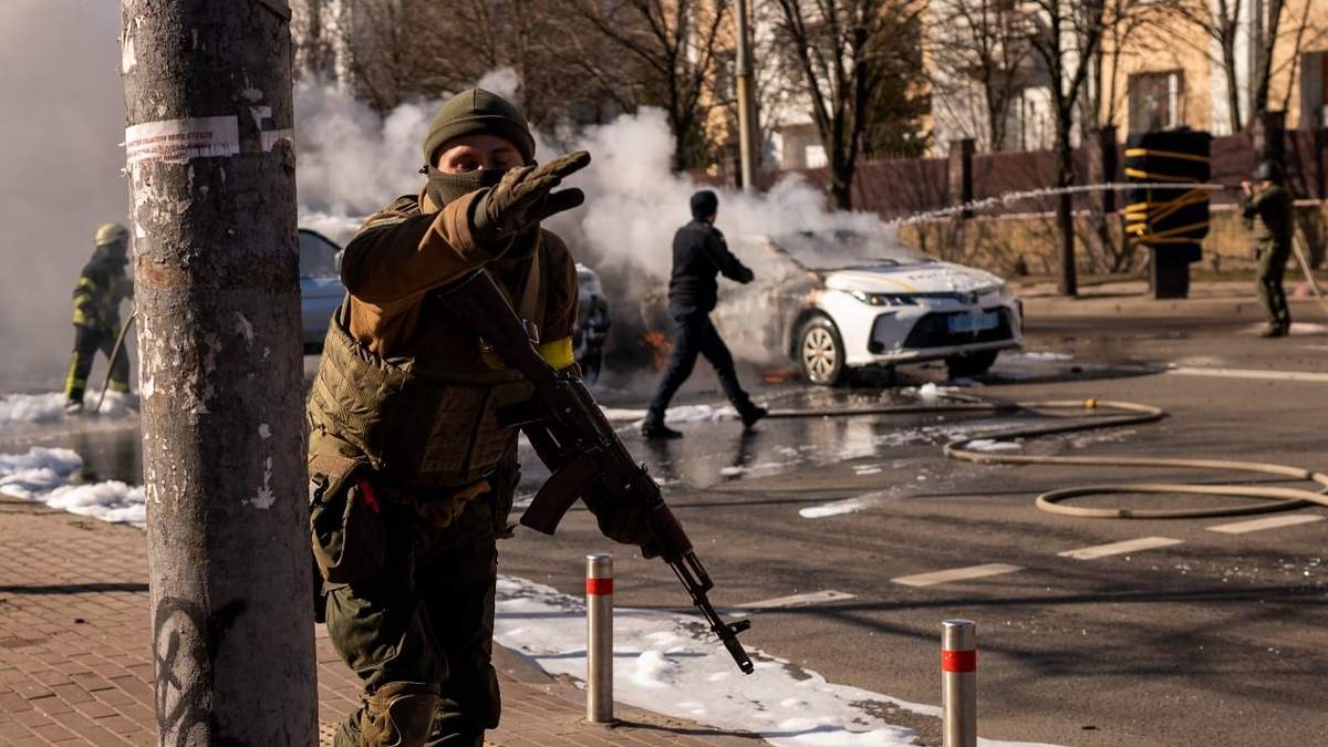Soldados ucranianos toman posiciones en torno a una instalación militar mientras arden dos automóviles en una calle en Kiev