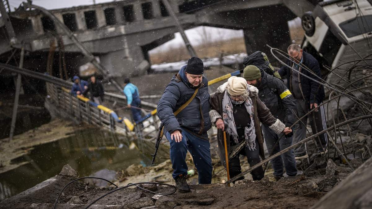Milicianos ayudan a una anciana a cruzar un puente destruido por la artillería rusa a las afueras de Kiev, Ucrania
