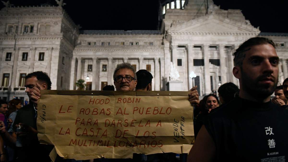 Personas protestan fuera del Congreso Nacional con un cartel de rechazo a las medidas económicas de Milei