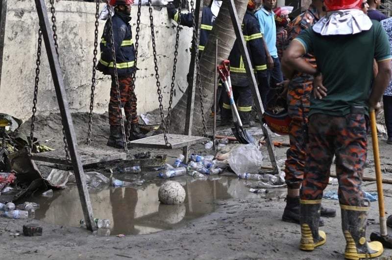 Bomberos junto a un columpio mientras trabajan en el lugar donde un avión de entrenamiento de la Fuerza Aérea de Bangladesh se estrelló contra un campus escolar poco después del despegue en Daca, Bangladesh, el lunes 21 de julio de 2025.