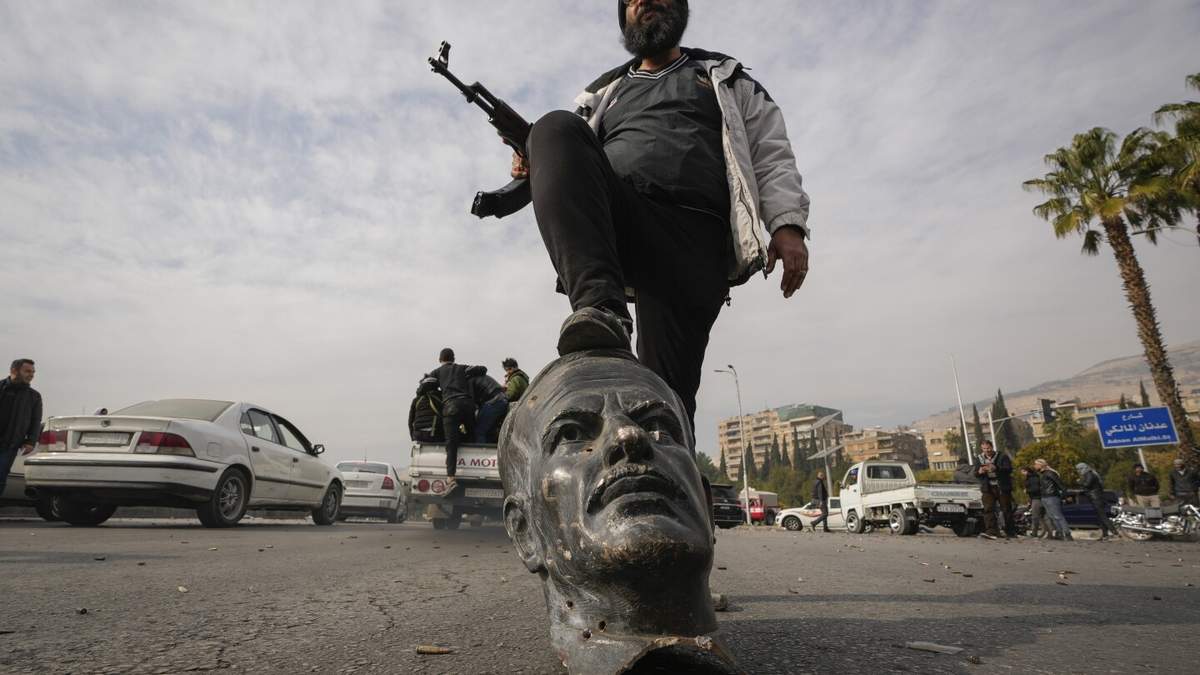 Un rebelde sirio sobre un busto de fallecido presidente sirio Hafez Assad en Damasco