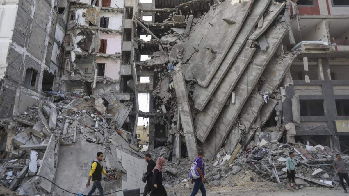 Palestinos caminan frente a edificios impactados por ataques israelíes en Ciudad de Gaza, el viernes 24 de noviembre de 2023