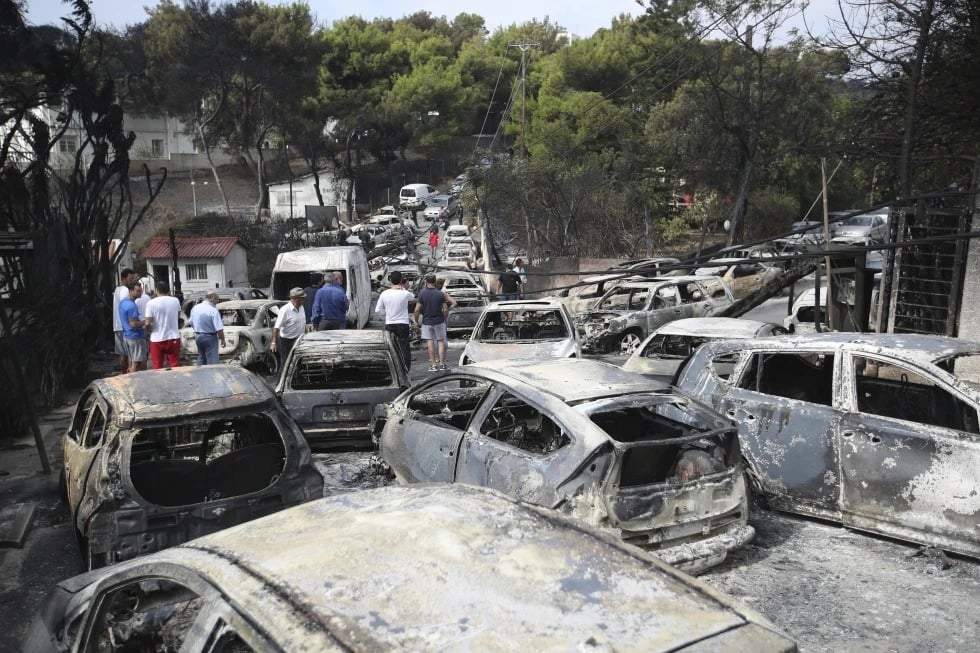 Personas observan los restos carbonizados de autos quemados en Mati, al este de Atenas, el martes 24 de julio de 2018.