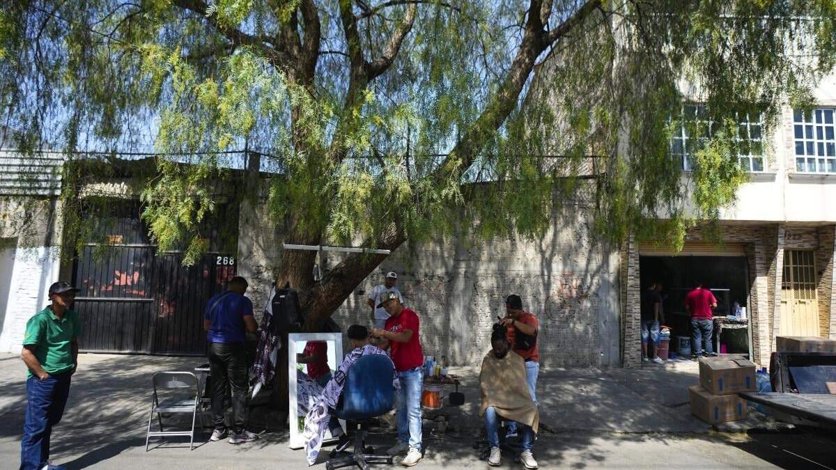 Migrantes venezolanos se cortan el pelo junto a las vías del tren bordeadas por tiendas de campaña improvisadas en la Ciudad de México