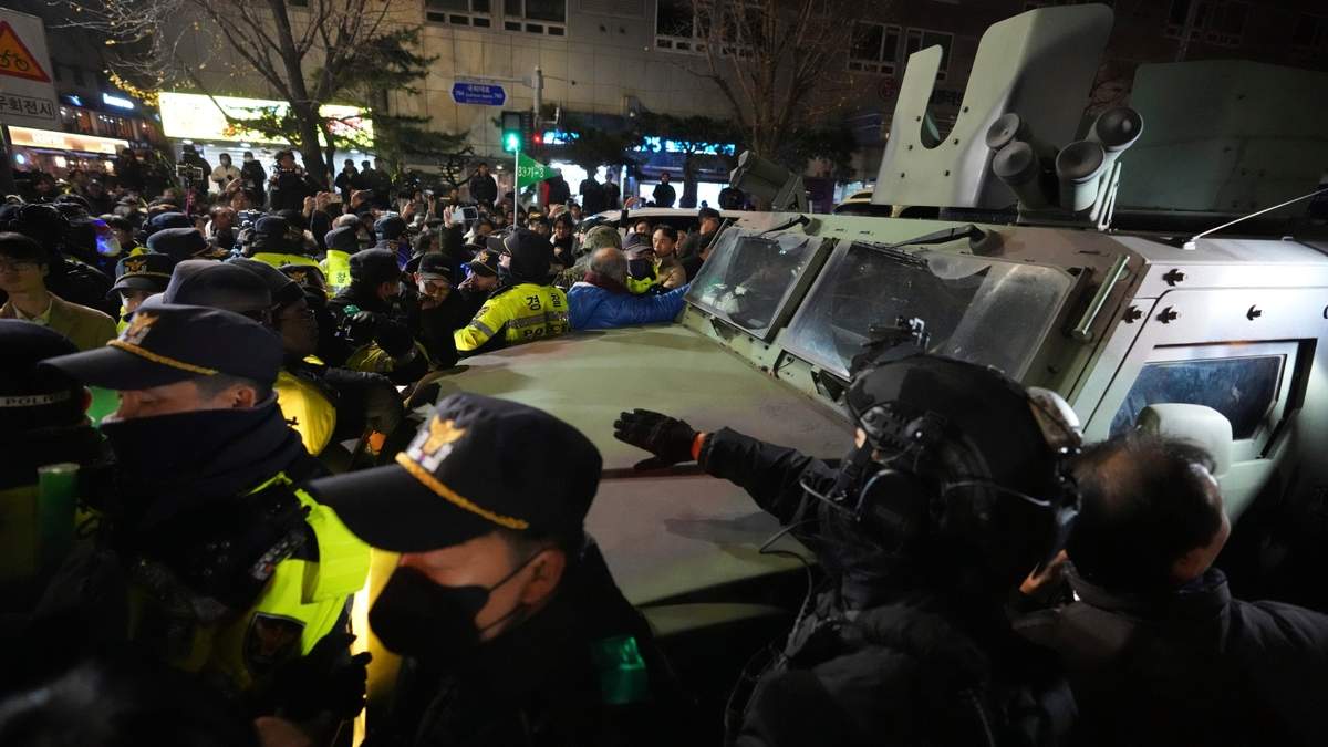 Un vehículo militar es escoltado por agentes de policía mientras la gente intenta bloquear el paso a la Asamblea Nacional en Seúl