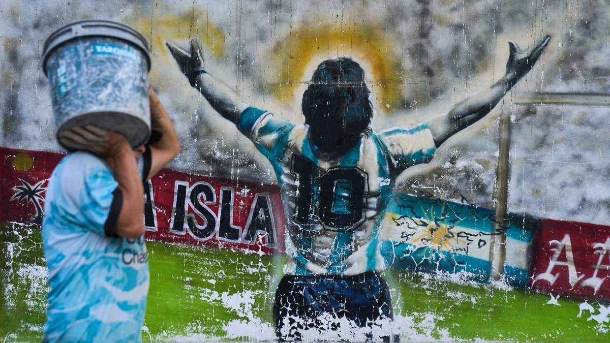 Un peatón pasa con un cubo junto a un grafiti que representa al fallecido futbolista Diego Maradona en Buenos Aires, Argentina, el lunes 13 de abril de 2026