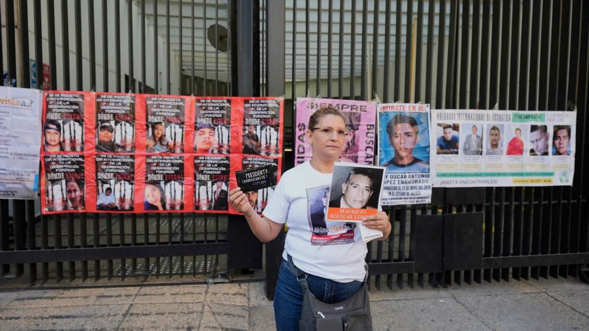 Una mujer muestra la foto de un desaparecido en frente de la puerta del Senado, cubierta de imágenes de personas desaparecidas, en Ciudad de México