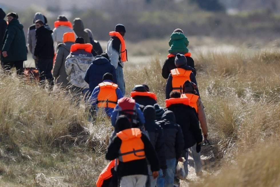 Migrantes que intentan llegar a Gran Bretaña caminan por la orilla de una playa en Gravelines, al norte de Francia, el miércoles 18 de marzo de 2026.
