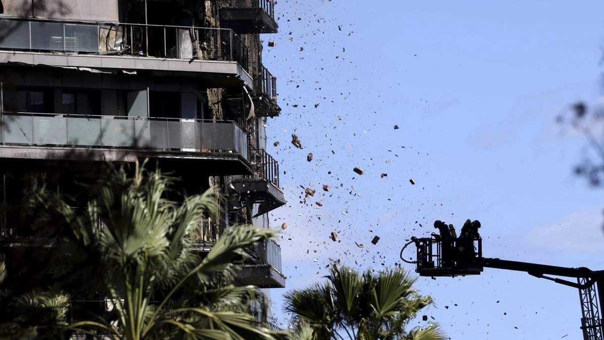 Escombros caen frente a los bomberos que realizan tareas en un edificio de apartamentos incendiado en Valencia, España
