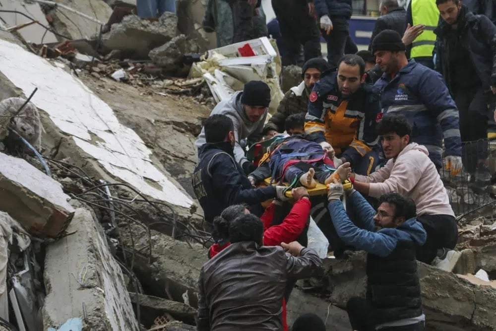 Gente y equipos de rescatistas trasladan a una persona en camilla desde un edificio derruido en Adana, Turquía, el 6 de febrero de 2023
