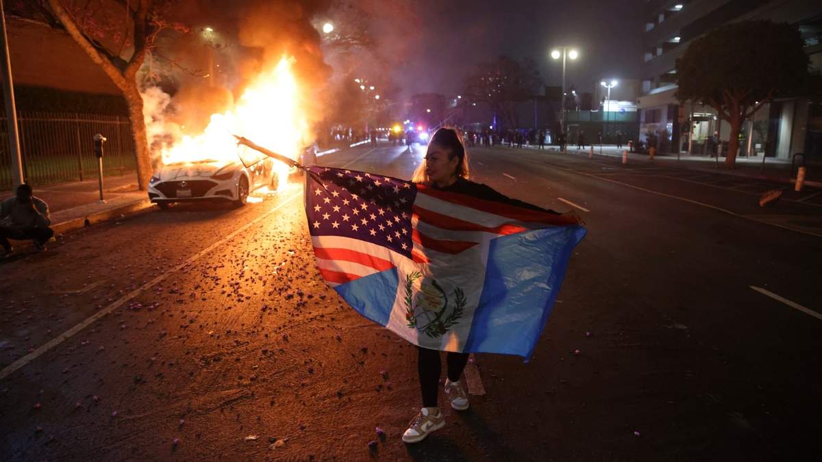 Un manifestante pasa junto a un coche en llamas durante las protestas contra las redadas migratorias del gobierno de Trump en Los Ángeles