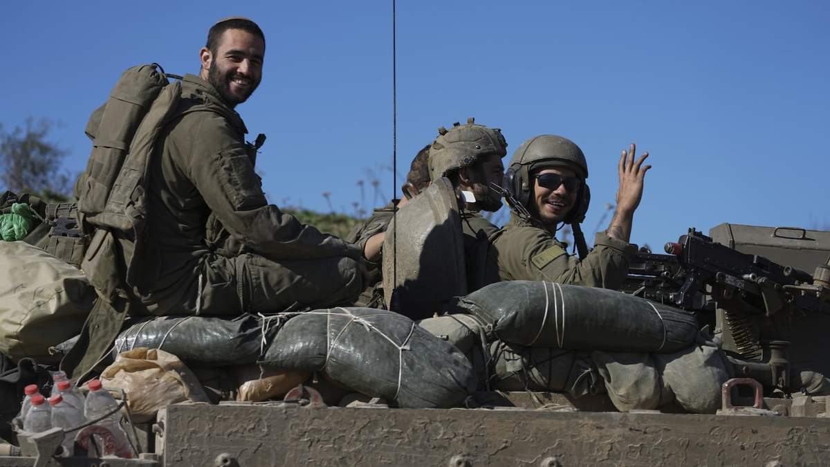 Soldados israelíes saludan a cámara desde un vehículo de transporte blindado mientras cruzan desde la Franja de Gaza a Israel