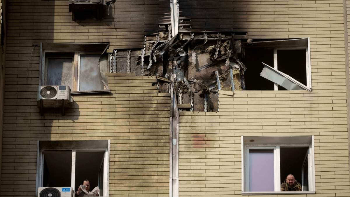 Un hombre mira mientras su vecina limpia un apartamento dañado en un edificio de viviendas de varias plantas tras un ataque de don ruso durante la noche en Kiev, Ucrania