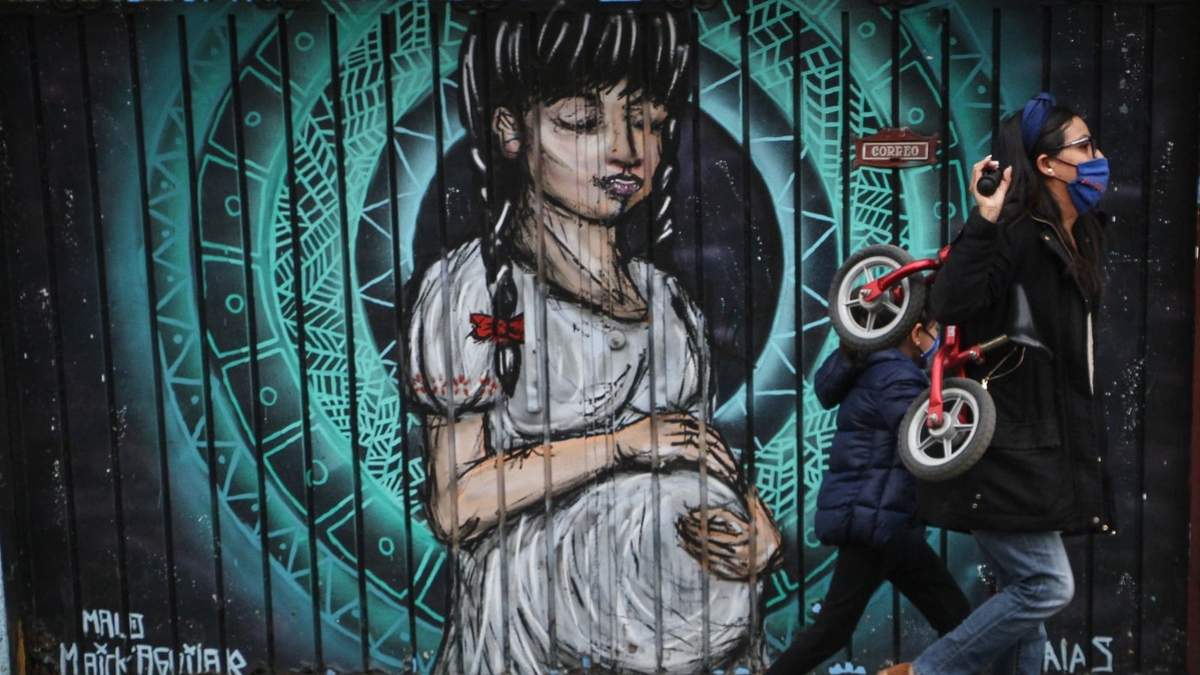 Una mujer con su hijo pasan junto a una imagen de una embarazada