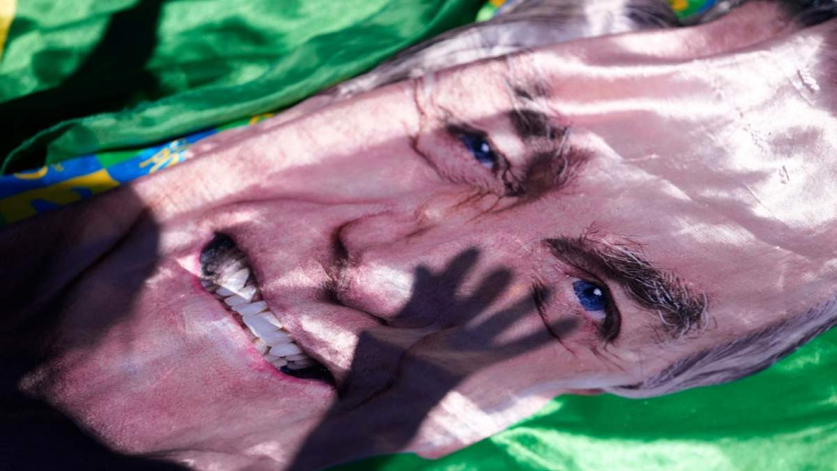 La sombra de un partidario del expresidente Jair Bolsonaro se proyecta sobre una imagen suya expuesta fuera del hospital al que fue trasladado desde la prisión para ser operado