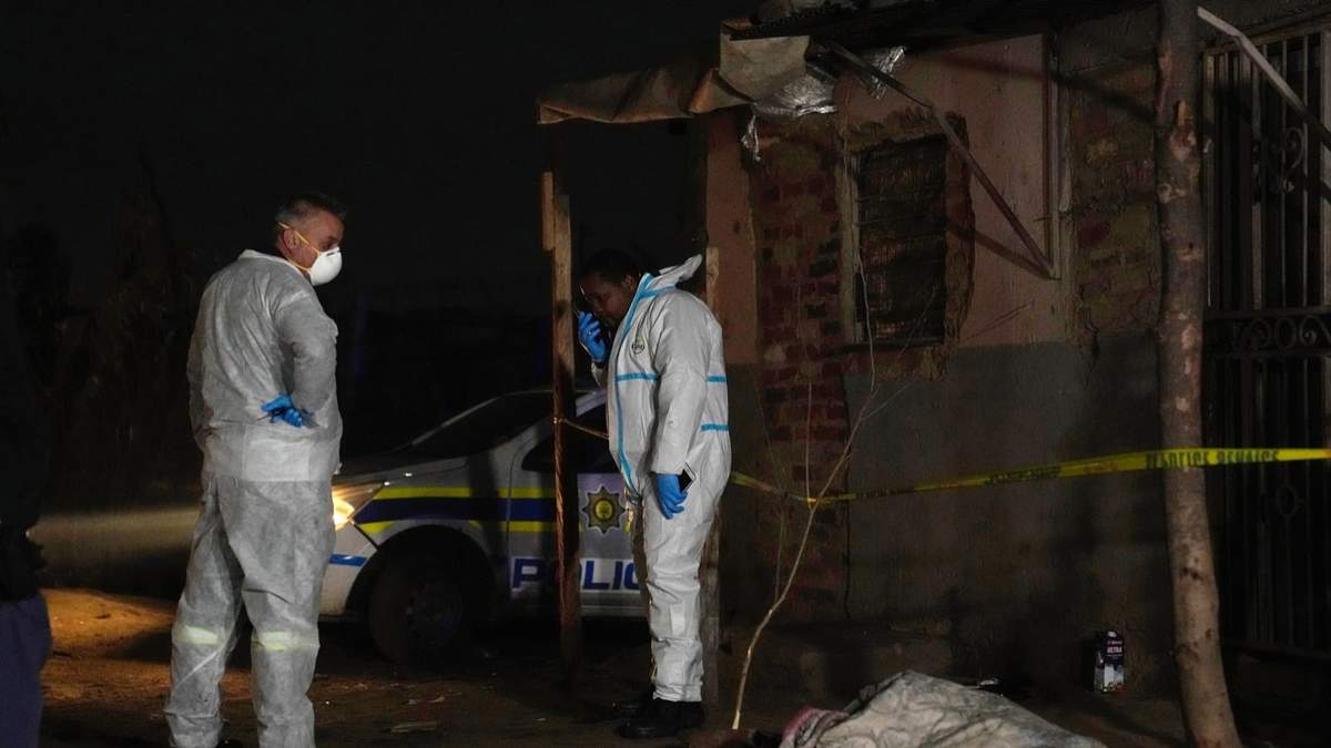 Dos policías permanecen cerca de un cadáver en el asentamiento Angelo el jueves 6 de julio de 2023, en Boksburg, Sudáfrica