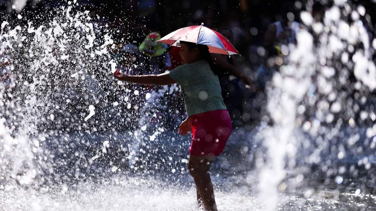 Una niña se cubre de los rayos del sol con una gorra de sombrilla mientras juega en una fuente de la Alameda Central debido a la ola de calor
