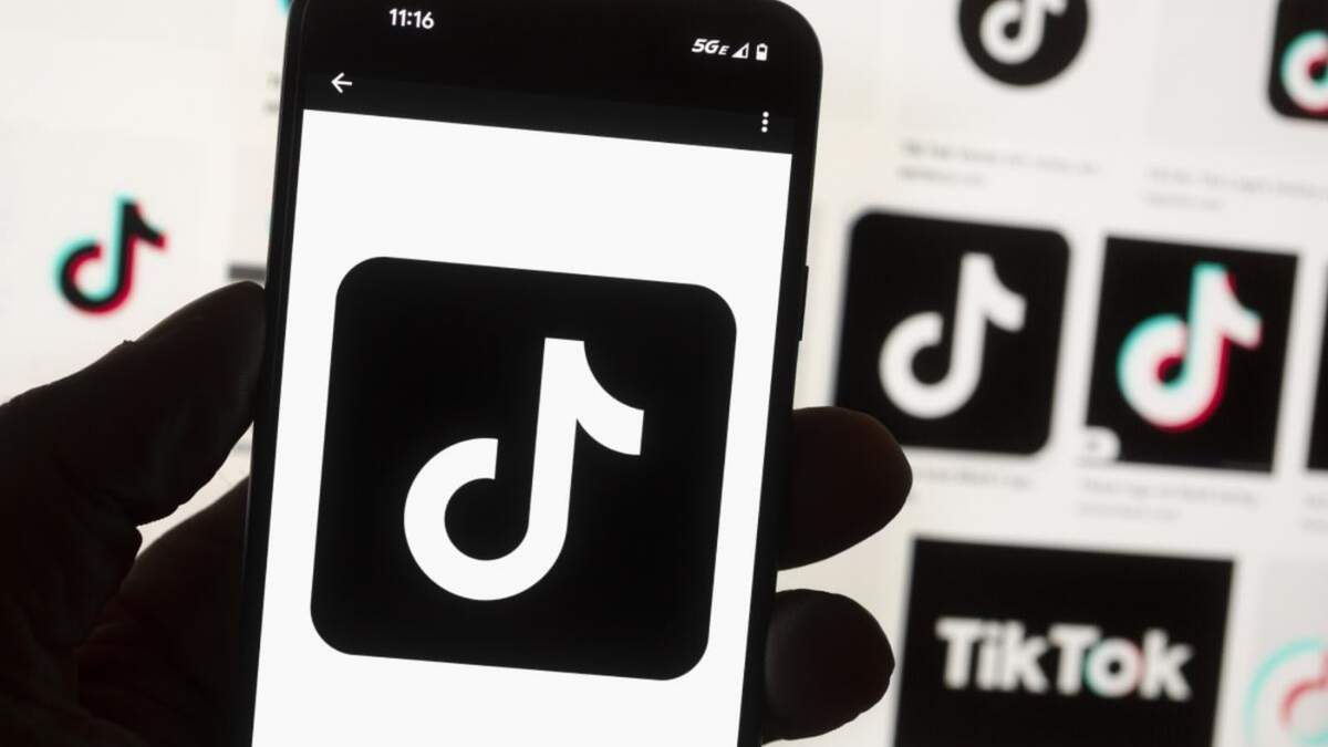 El logotipo de TikTok aparece en la pantalla de un teléfono celular frente al monitor de una computadora