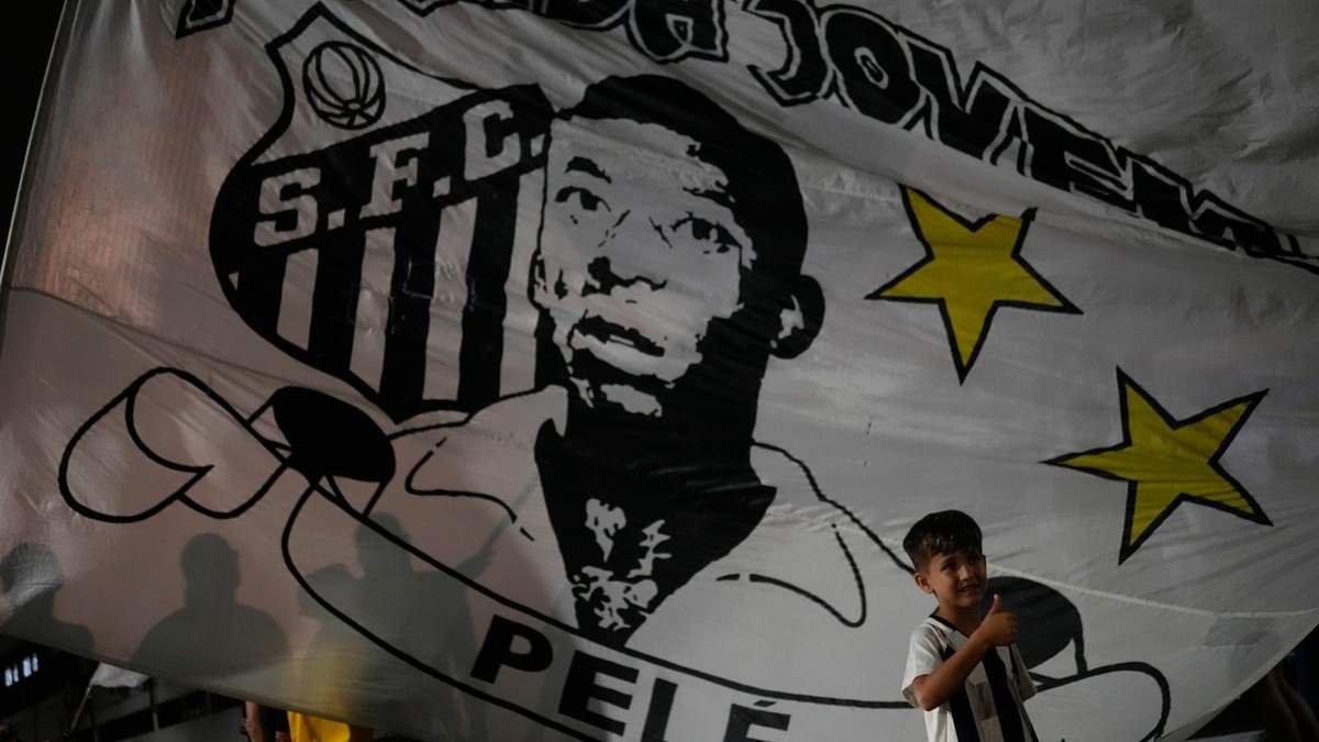 Un niño posa frente a una bandera de Pelé afuera del estadio Vila Belmiro, sede del club de futbol Santos