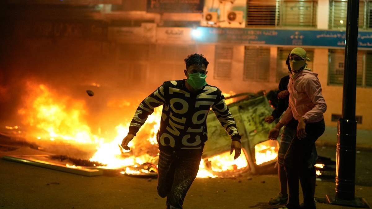 Una persona corre junto a un vehículo policial incendiado durante las protestas lideradas por jóvenes que exigían reformas sanitarias y educativas en Salé, Marruecos