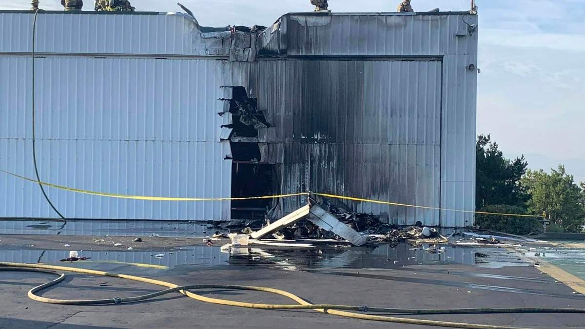 Bomberos examinan un hangar dañado por un avión pequeño que se estrelló contra él