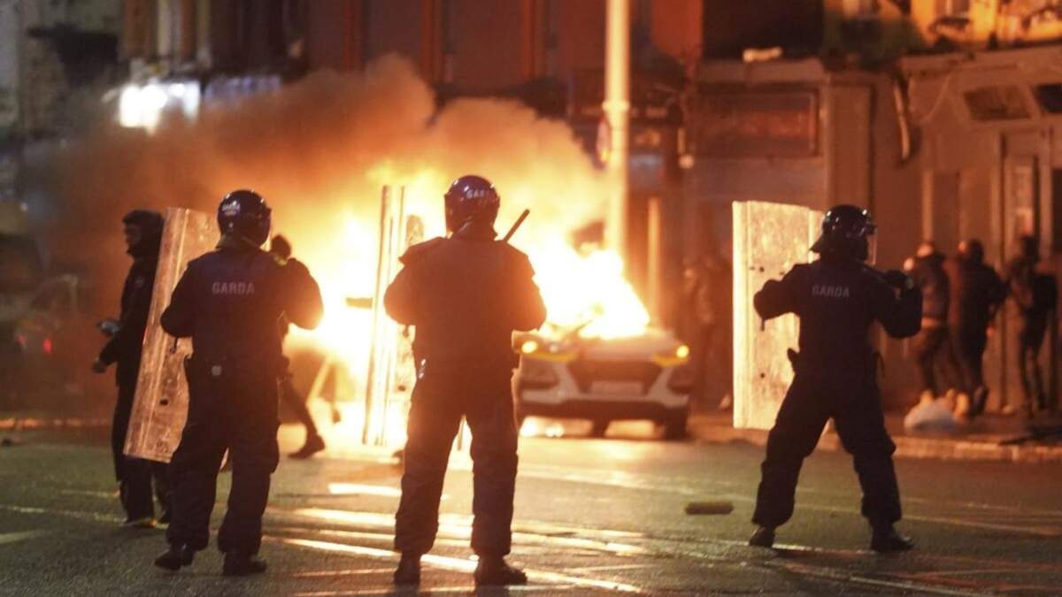 Un auto arde ante la presencia de agentes de la policía irlandesa en la escena de un ataque, en Dublín, Irlanda