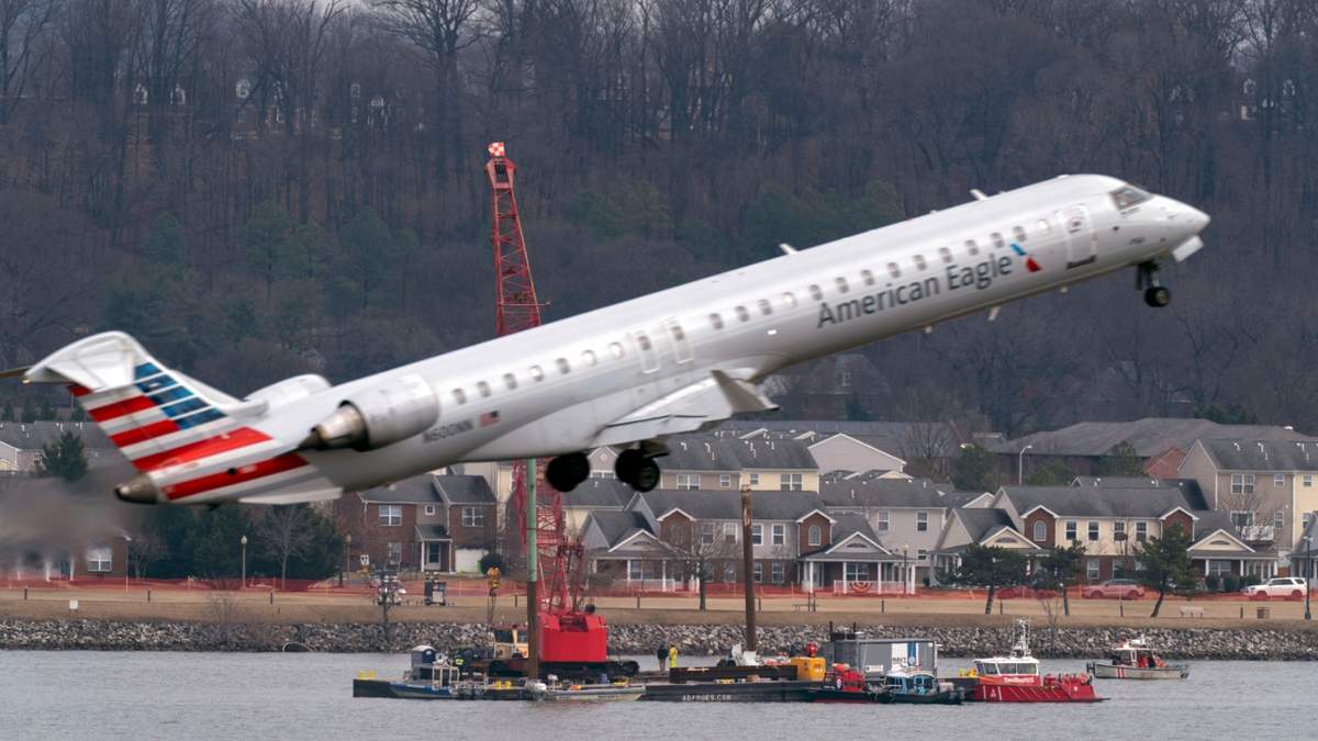 Mientras un avión de American Eagle despega, cuadrillas realizan tareas de recuperación cerca del punto en el río Potomac donde cayeron los restos de un avión comercial y un helicóptero militar que chocaron en pleno vuelo en el Aeropuerto Nacional Ronald Reagan, el jueves 6 de febrero de 2025, en Arlington, Virginia