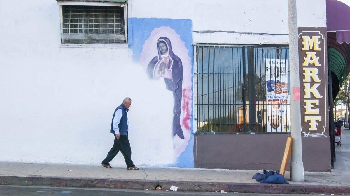 En esta fotografía de Oscar Rodriguez Zapata, un hombre camina al lado de un mural de la Virgen de Gualupe parcialmente cubierto con pintura en una pared en Los Ángeles, en 2018