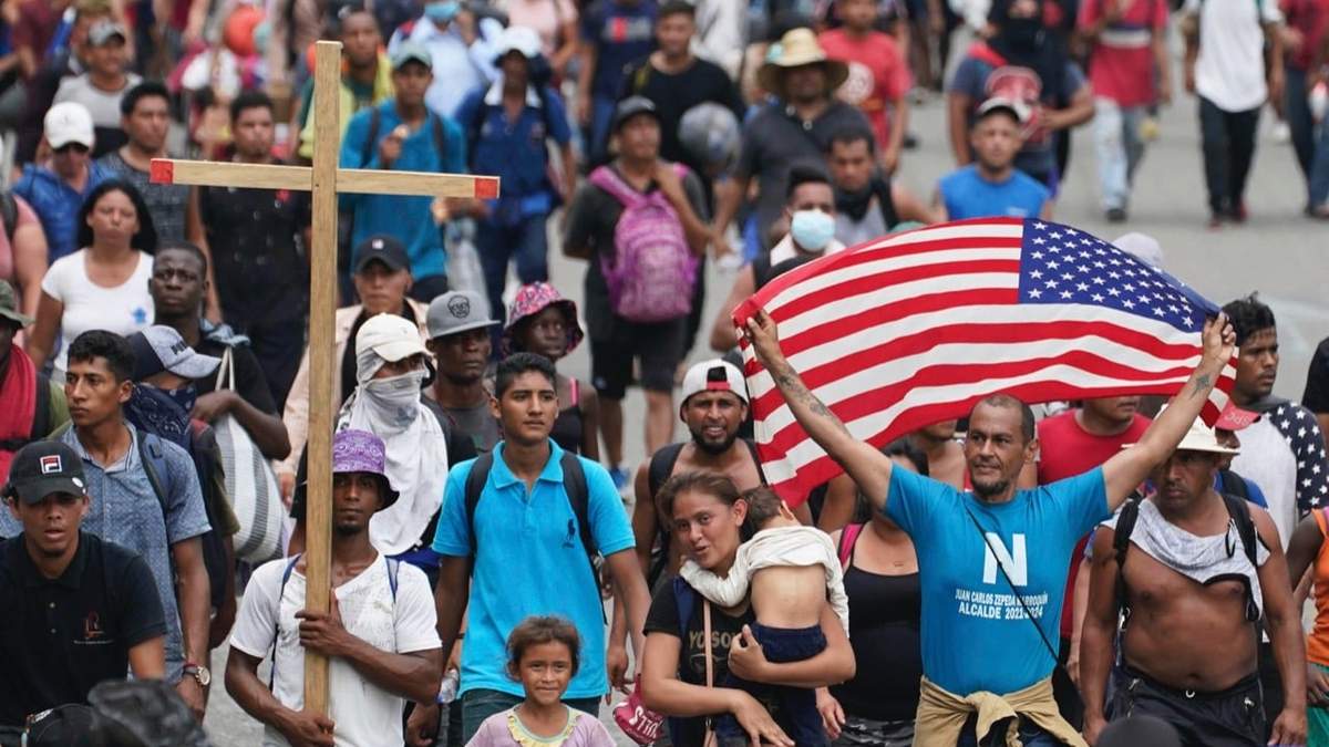 Un migrante ondea la bandera de EU mientras camina por una carretera costera en las afueras de Huixtla