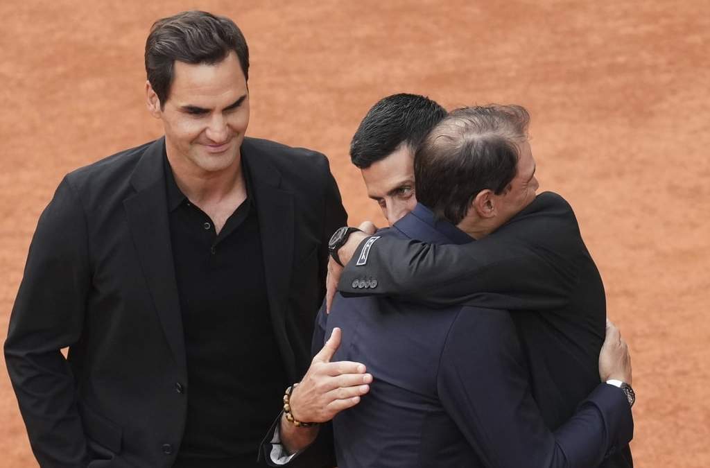 Roger Federer observa mientras Novak Djokovic y Rafael se abrazan en la pista de la cancha Philippe-Chatrier