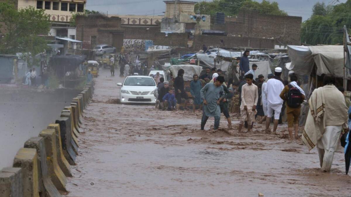 Gente vadeando un puente inundado junto a un arroyo desbordado por las lluvias, a las afueras de Peshawar, Pakistán