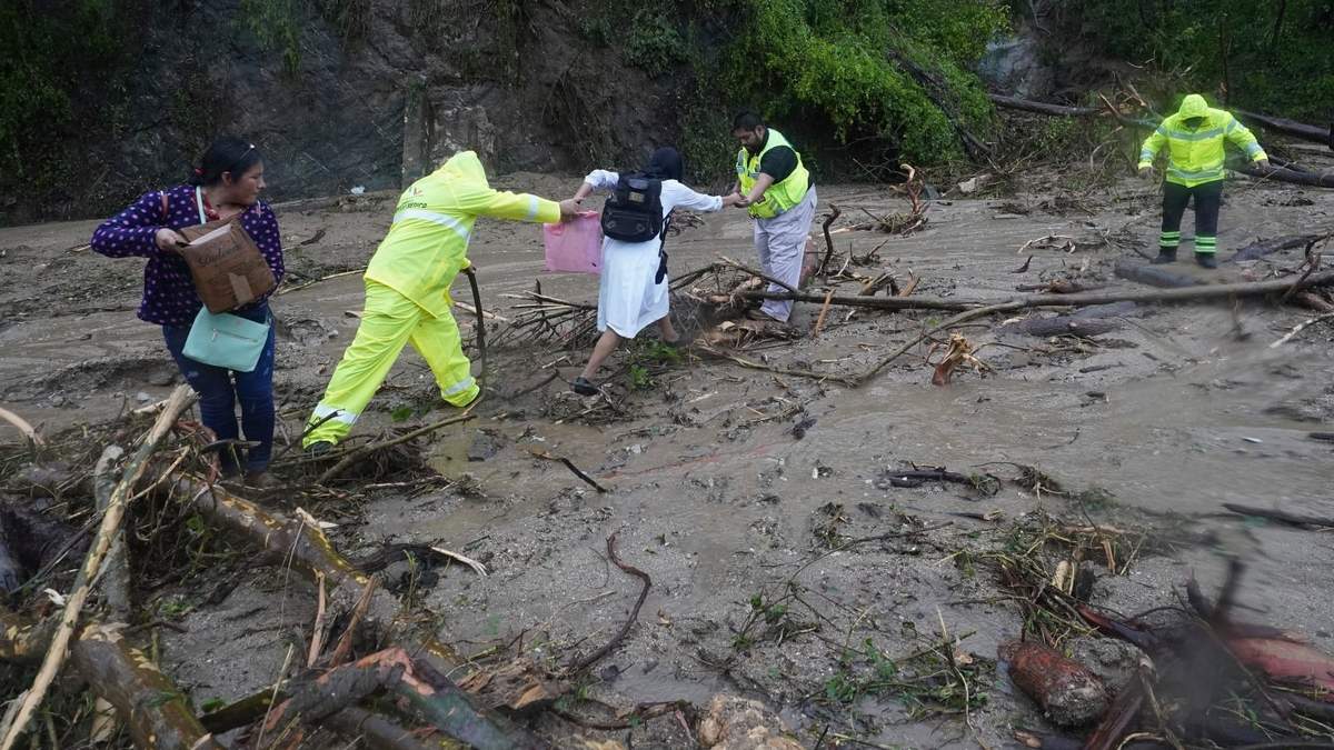 La gente recibe ayuda para cruzar una carretera bloqueada por un deslizamiento de tierra provocado por el huracán Otis cerca de Acapulco