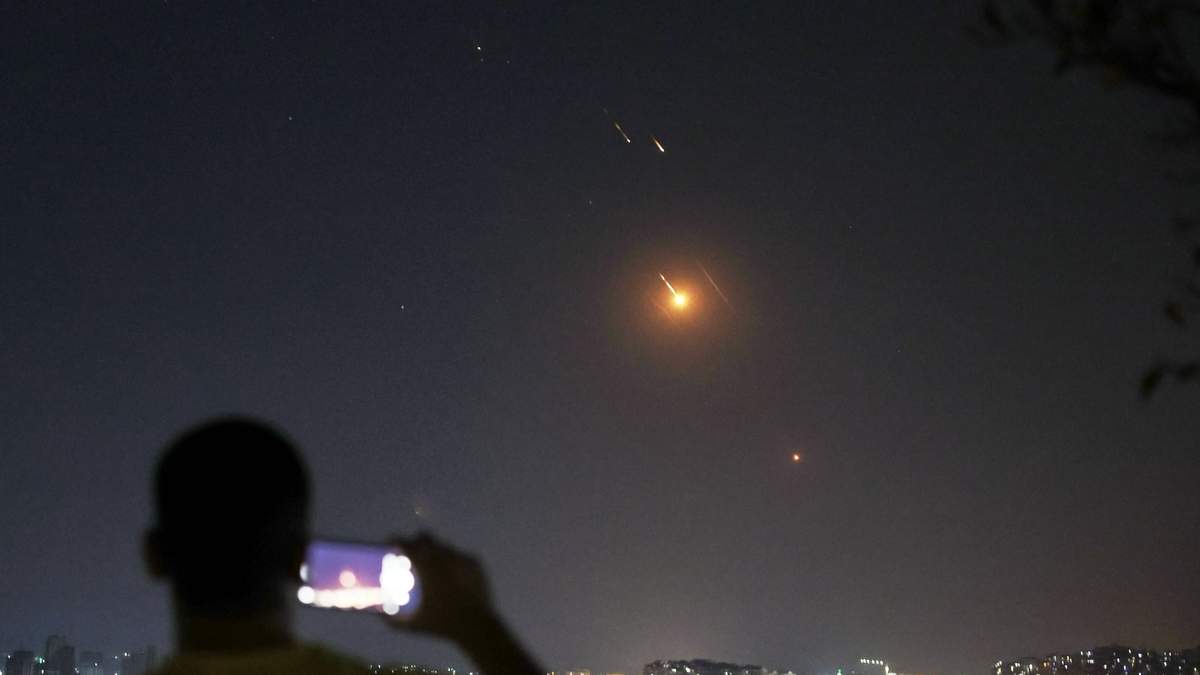 Un hombre toma una foto con su celular mientras misiles disparados desde Irán hacia Israel sobrevuelan territorio sirio en Damasco, Siria