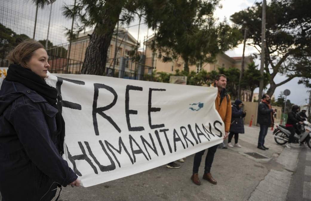 Defensores de los 24 trabajadores humanitarios que están acusados de participar en operativos de rescate de migrantes sostienen un letrero afuera del tribunal de Mitilene, en la isla de Lesbos, Grecia