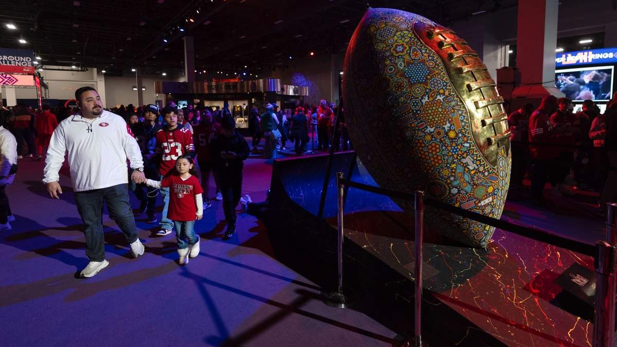Aficionados caminan junto a una escultura de un balón de fútbol americano decorado en el NFL Experience en Las Vegas
