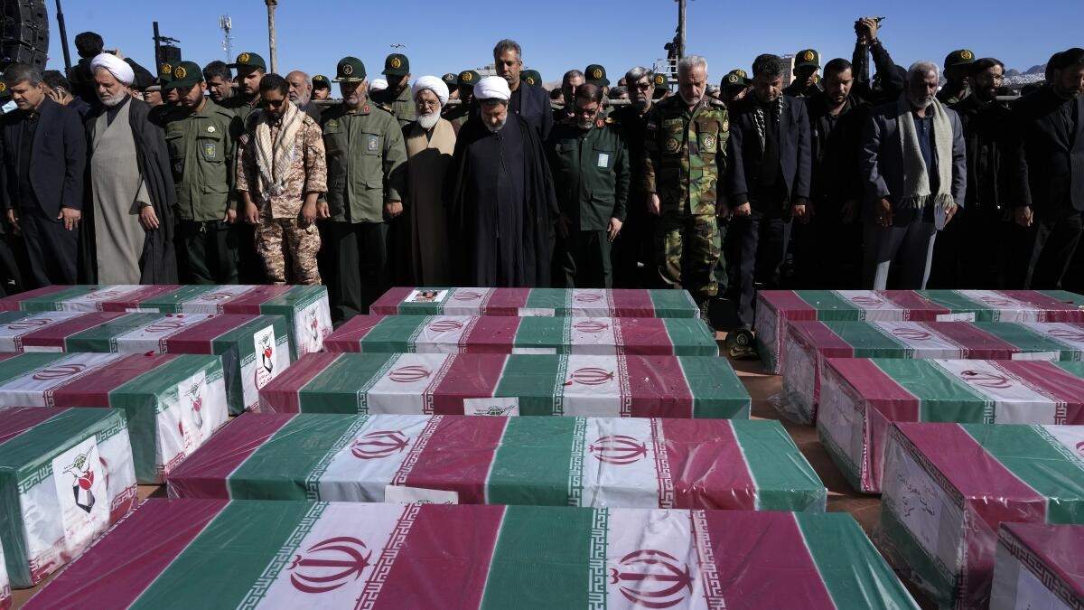 Varias personas rezan junto a los ataúdes, cubiertos con banderas de Irán, de las víctimas de un atentado, durante su funeral en la ciudad de Kermán, a unos 820 kms (510 millas) al sureste de la capital, Teherán