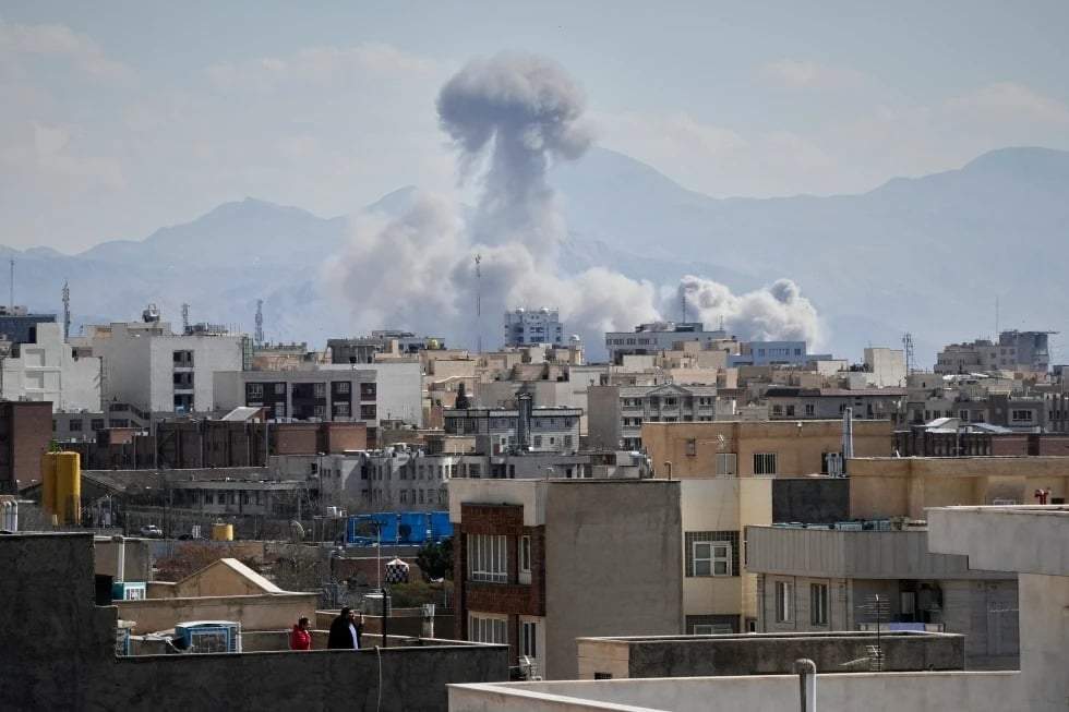 La gente observa desde una azotea cómo se eleva una columna de humo tras un ataque en Teherán, Irán, el domingo 1 de marzo de 2026.