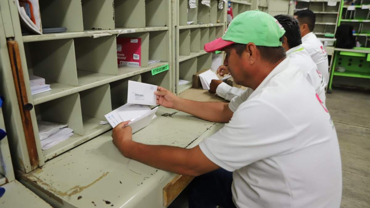 Trabajadores de Correos de México sentados mientras trabajan