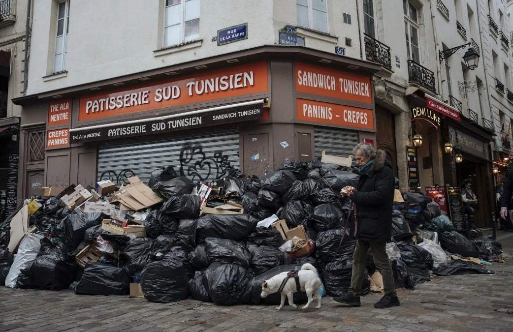 Un hombre pasa caminando junto a montones de basura en París