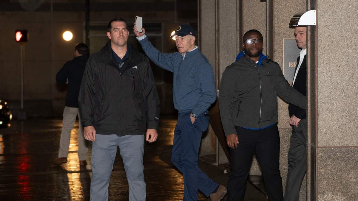 El presidente Joe Biden saluda mientras agentes del Servicio Secreto lo protegen a su salida de su sede de campaña en Wilmington, Delaware