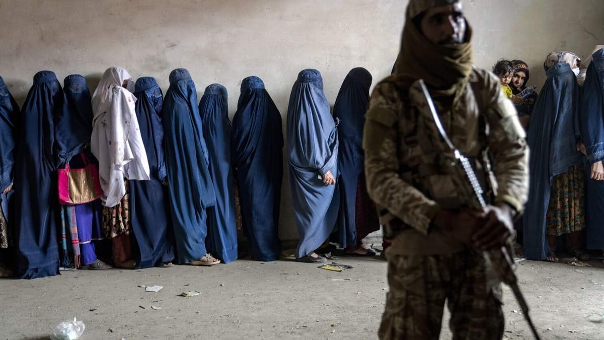 ARCHIVO -Un combatiente talibán monta guardia mientras varias mujeres esperan a recibir raciones de comida distribuidas por un grupo humanitario en Kabul, Afganistán